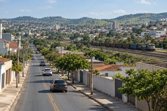 Ilustração de rua urbana próxima a um corredor ferroviário de cargas em uma cidade de relevo ondulado.