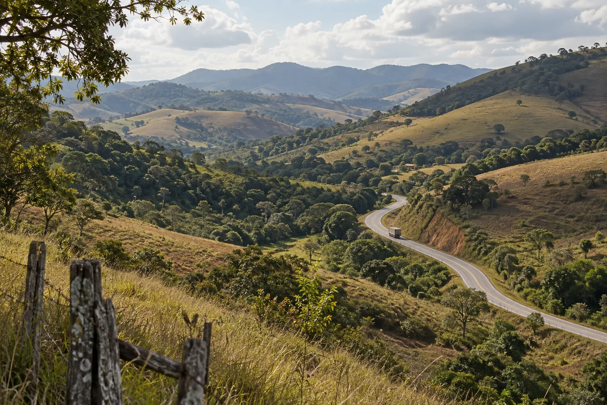 Rodovia sinuosa em um vale de colinas, pastagens e matas, com um caminhão distante, em composição ilustrativa.