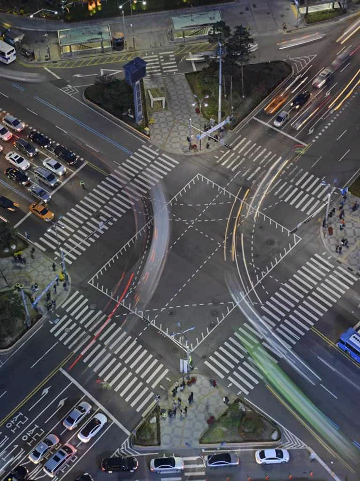 Vista aérea noturna de uma interseção urbana com faixas de pedestres e fluxos de veículos