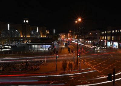 Uma rua da cidade à noite com sinais de trânsito e edifícios ao fundo e um poste de luz no primeiro plano com um sinal de trânsito no meio, (uma foto do tipo tilt shift: 0,198).