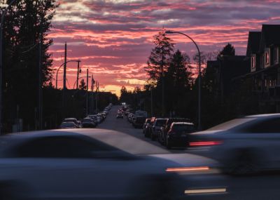 Uma rua cheia de tráfego sob um céu colorido ao pôr do sol com carros circulando pela rua e alguns prédios ao lado. (uma foto com efeito tilt shift: 0,159)