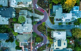 Uma estrada serpenteando por um bairro com casas e carros ao seu redor e uma rua com carros em ambos os lados e casas em ambos os lados. (uma foto de estoque: 0,279)