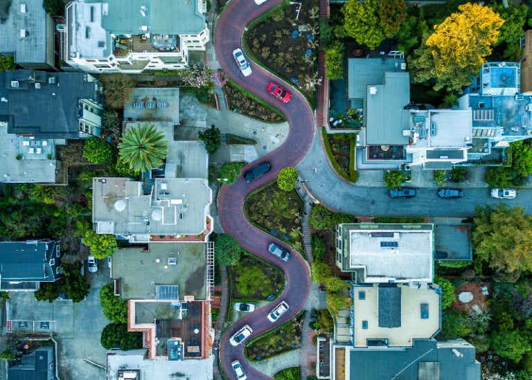 Uma estrada serpenteando por um bairro com casas e carros ao seu redor e uma rua com carros em ambos os lados e casas em ambos os lados. (uma foto de estoque: 0,279)