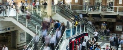 Um grupo de pessoas andando para cima e para baixo em um conjunto de escadas em um prédio com uma escadaria que leva a uma área de segundo andar, com um segundo piso, (uma foto em tilt shift: 0,241).
