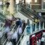 Um grupo de pessoas andando para cima e para baixo em um conjunto de escadas em um prédio com uma escadaria que leva a uma área de segundo andar, com um segundo piso, (uma foto em tilt shift: 0,241).