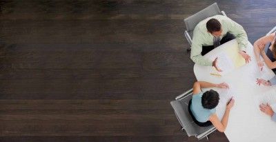 Um grupo de pessoas sentadas ao redor de uma mesa com papéis e laptops em cima, olhando para baixo para os papéis em uma mesa com cadeiras ao seu redor e um homem em pé na mesa. (uma foto de banco de imagens:0,542)