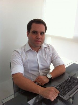 Um homem sentado em uma mesa com um computador portátil em seu colo, com as mãos nos joelhos, com um relógio no pulso esquerdo (um retrato de personagem: 0.307).