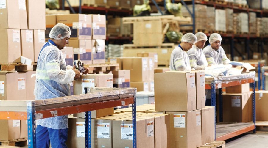 Um grupo de trabalhadores em um armazém com caixas e caixas nas prateleiras e um homem de camisa branca e calça azul e chapéu branco, (uma foto de estoque: 0,726)