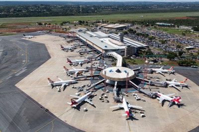 Um grande aeroporto com muitos aviões estacionados em sua área de estacionamento e um prédio terminal ao fundo com carros estacionados na área de estacionamento. (uma foto em tilt shift: 0,789)