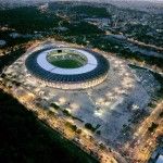 Um grande estádio com um grande telhado circular à noite, com luzes nele e muitas pessoas ao redor, no primeiro plano da cidade. (uma foto microscópica: 0,314)