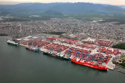 Um grande navio de carga ancorado em um porto com uma cidade ao fundo e montanhas ao longe, com um grande navio porta-contêineres vermelho em primeiro plano, (uma foto inclinada em miniatura:0,406)