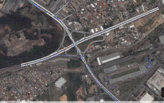 Uma grande intersecção com múltiplas faixas e uma estrada no meio, e um grande prédio ao fundo com grande quantidade de tráfego (uma foto em tilt shift: 0.395).