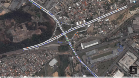 Uma grande intersecção com múltiplas faixas e uma estrada no meio, e um grande prédio ao fundo com grande quantidade de tráfego (uma foto em tilt shift: 0.395).