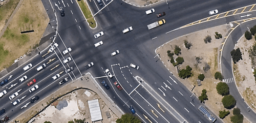 Uma vista aérea de um cruzamento movimentado com carros e caminhões em seus lados e uma rua com uma luz amarela no topo do cruzamento, (uma fotografia tilt shift: 0,275).