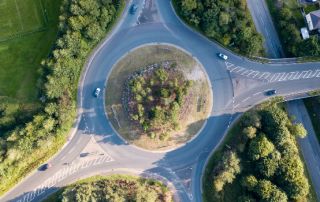 Uma interseção de estrada com um carro dirigindo nela e uma estrada atravessando pelo meio de uma área de parque com árvores e grama em ambos os lados, (uma foto de estoque: 0,471)