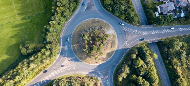 Uma interseção de estrada com um carro dirigindo nela e uma estrada atravessando pelo meio de uma área de parque com árvores e grama em ambos os lados, (uma foto de estoque: 0,471)