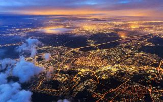 Uma vista de uma cidade a partir de um avião durante a noite, com nuvens e luzes no chão e as luzes da cidade ao longe, (uma foto microscópica: 0,178).