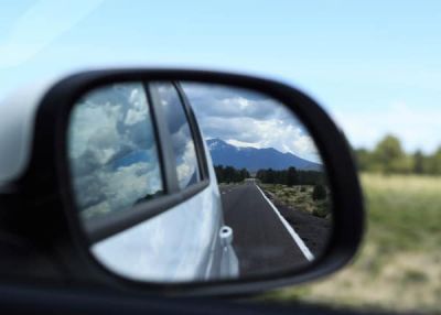 O espelho lateral de um carro reflete uma cadeia de montanhas no espelho retrovisor de um carro em uma estrada no campo. No espelho de vista lateral, há um carro (uma imagem de estoque: 0,496).