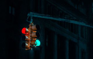 Um semáforo pendurado em um poste na escuridão, com um prédio ao fundo durante a noite, com uma luz verde no poste e uma luz vermelha. (uma foto: 0,123)
