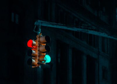 Um semáforo pendurado em um poste na escuridão, com um prédio ao fundo durante a noite, com uma luz verde no poste e uma luz vermelha. (uma foto: 0,123)