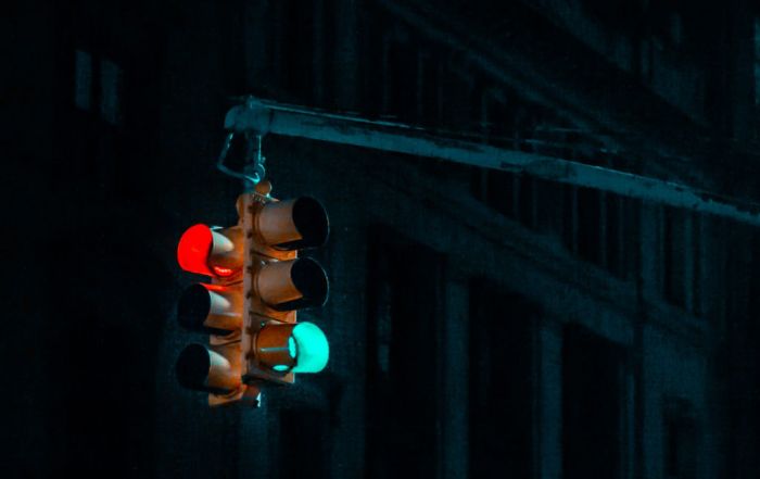 Um semáforo pendurado em um poste na escuridão, com um prédio ao fundo durante a noite, com uma luz verde no poste e uma luz vermelha. (uma foto: 0,123)