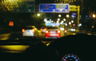 Uma visão de uma rua da cidade à noite, vista através do para-brisa de um carro com chuva nele e um velocímetro em primeiro plano com um fundo borrado. (uma foto de estoque: 0,206)
