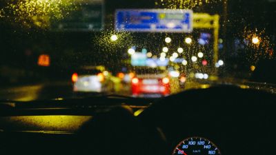 Uma visão de uma rua da cidade à noite, vista através do para-brisa de um carro com chuva nele e um velocímetro em primeiro plano com um fundo borrado. (uma foto de estoque: 0,206)