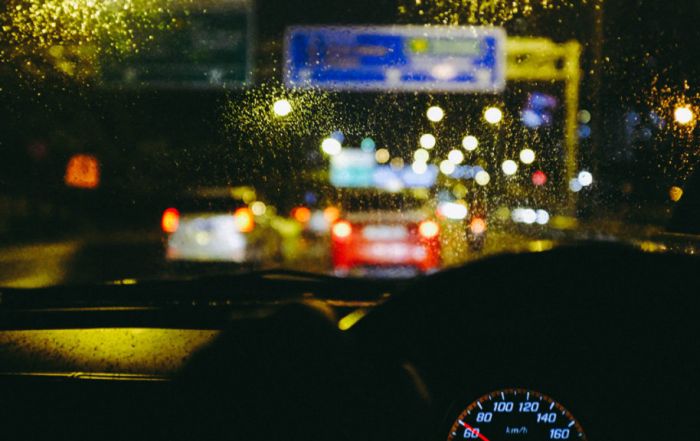 Uma visão de uma rua da cidade à noite, vista através do para-brisa de um carro com chuva nele e um velocímetro em primeiro plano com um fundo borrado. (uma foto de estoque: 0,206)