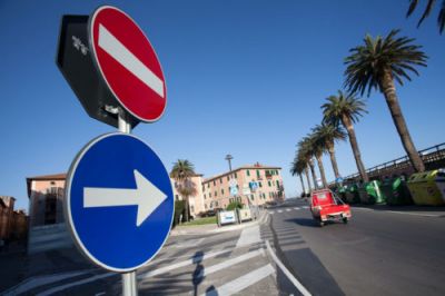 Uma placa de rua com uma seta vermelha apontando para a esquerda e uma seta azul apontando para a direita em uma rua com palmeiras e uma van vermelha, (uma foto de estoque: 0,353)
