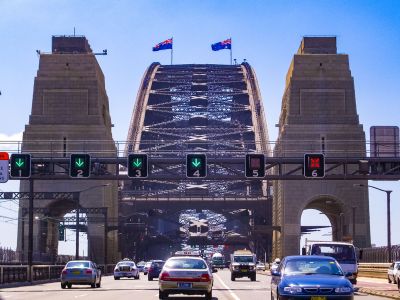 Uma ponte com tráfego passando por cima dela e um semáforo acima dela com bandeiras tremulando acima dela e um carro dirigindo na estrada abaixo dela e uma ponte, (uma pintura fosca:0,300)